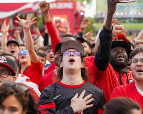 Canadian fans in red raise their fists and cheer at a World Cup fan festival, one with hand over chest